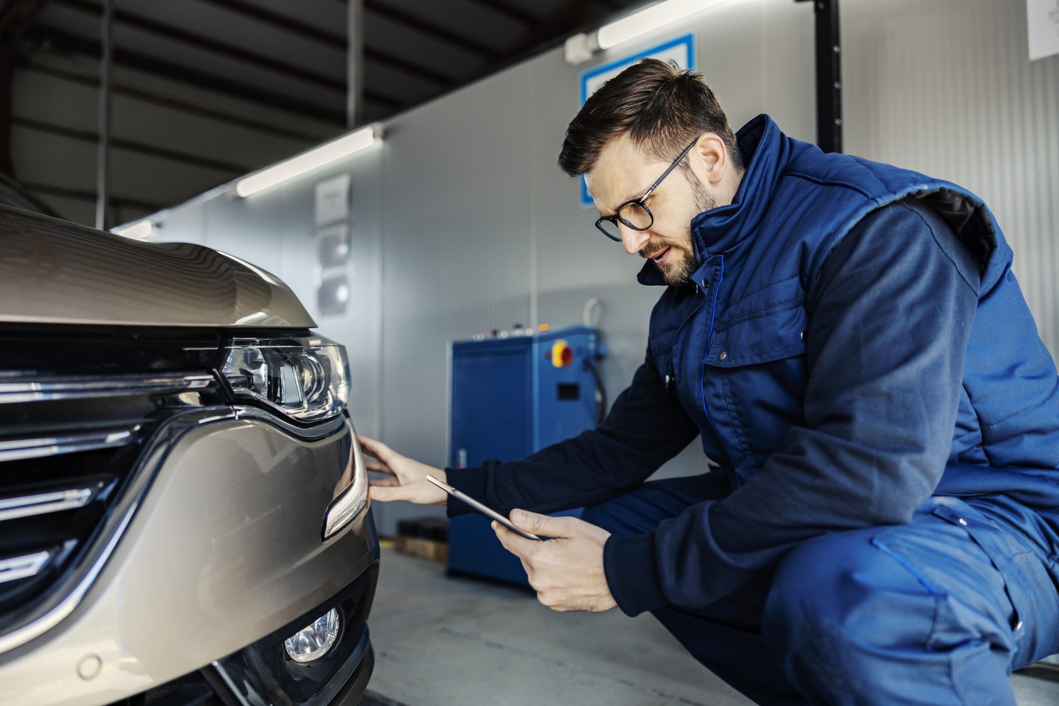 An inspector kneeling and does technical inspection of car at workshop.